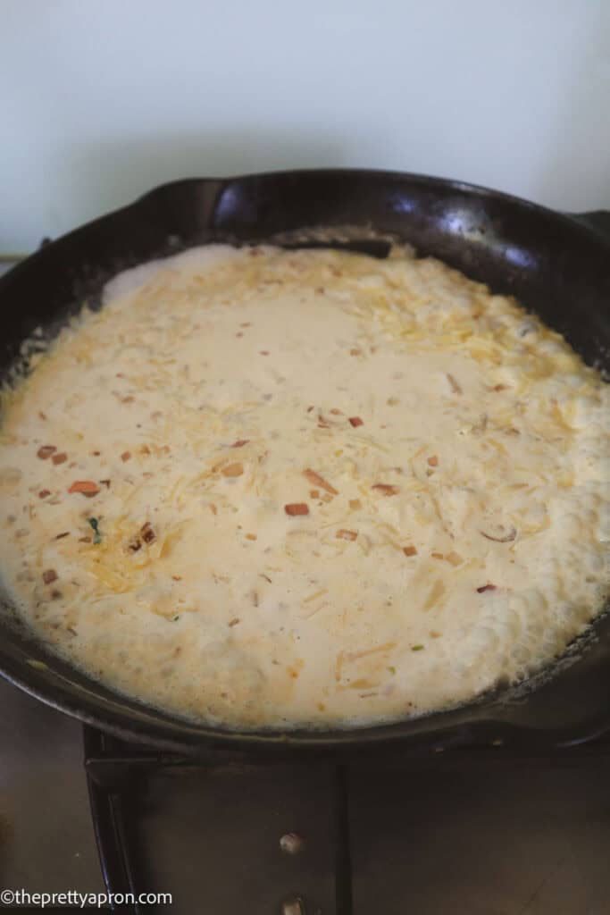 cream, shallots and parmesan boiling in black skillet