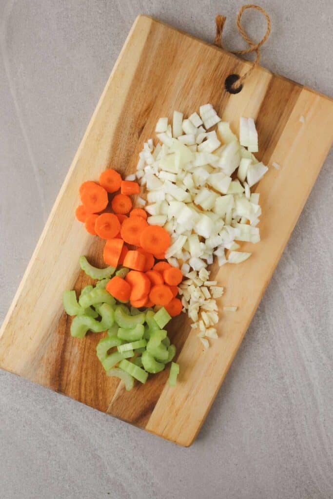 Chopped celery, carrots, onions and garlic on wooden cutting board