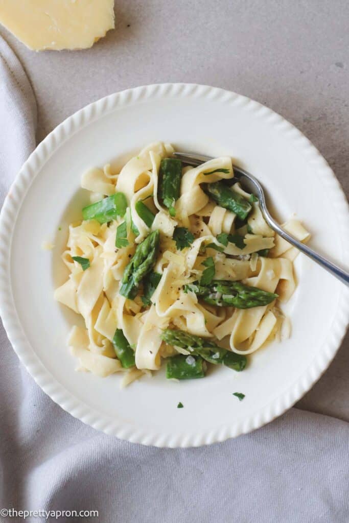 Pasta alfredo with asparagus in white bowl with a fork