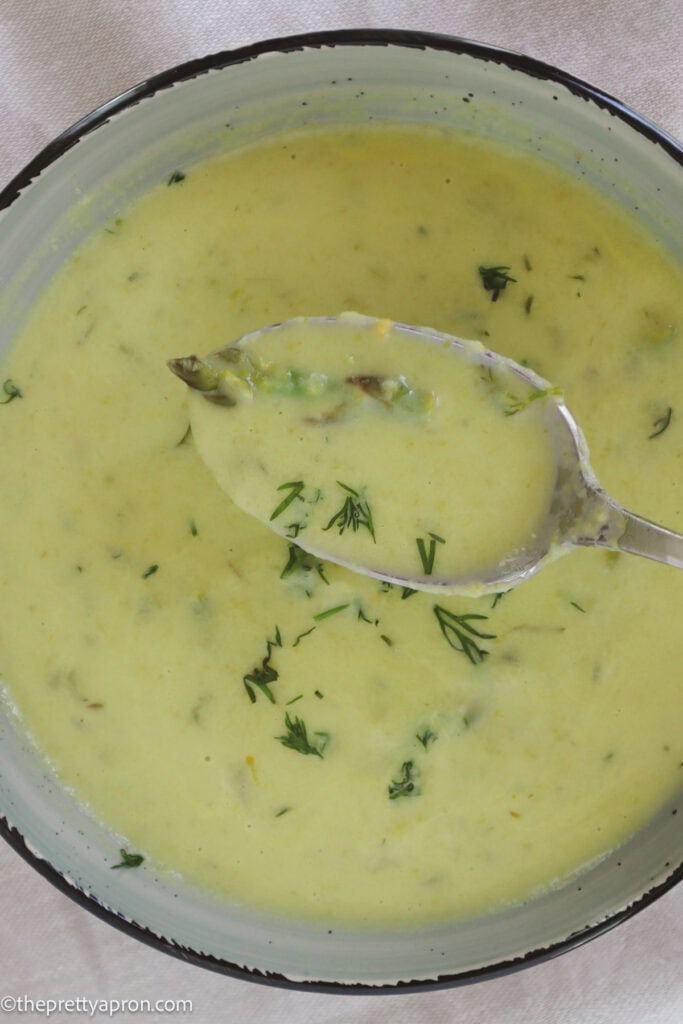 Asparagus dill soup in bowl with spoonful of creamy soup and dill scattered on top