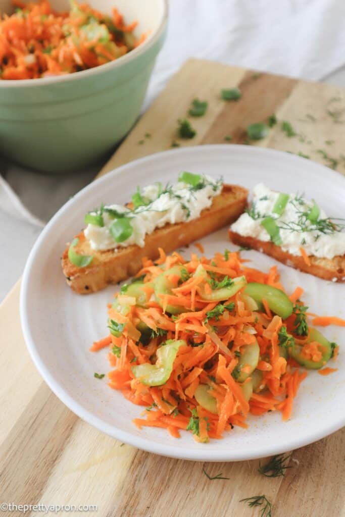 Carrots cucumber salad and two bruschettas on white plate with bowl of carrots and cucumber salad in background.