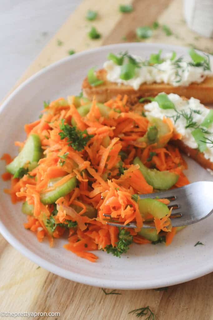 Forkful of Carrots cucumber salad on plate with two bruschettas with lemon ricotta dip and dill and spring onion