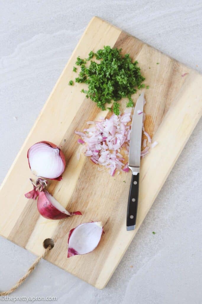 Chopped red onion and parsley on a cutting board.