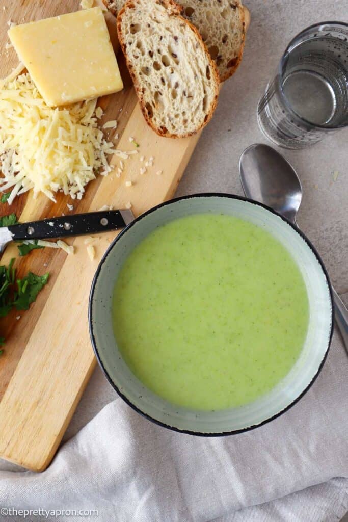 Creamy broccoli asparagus soup in bowl with sourdough bread, grated parmesan cheese, parsley and spoon
