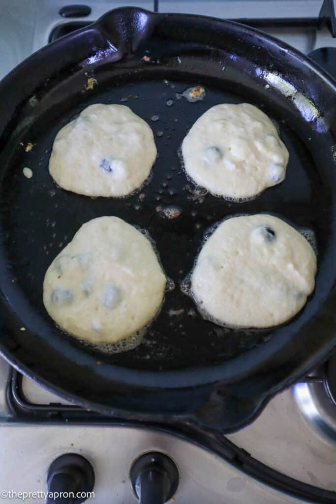 Four lemon ricotta blueberry pancakes cooking on black skillet