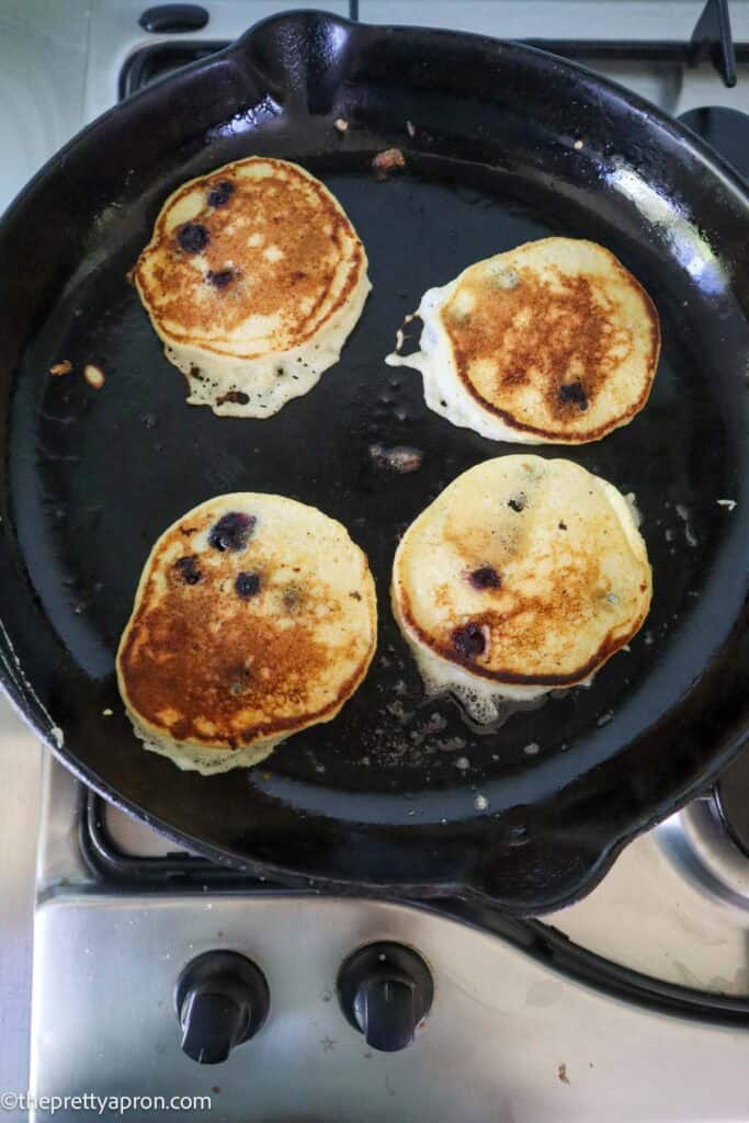 Four lemon ricotta blueberry pancakes flipped on black skillet