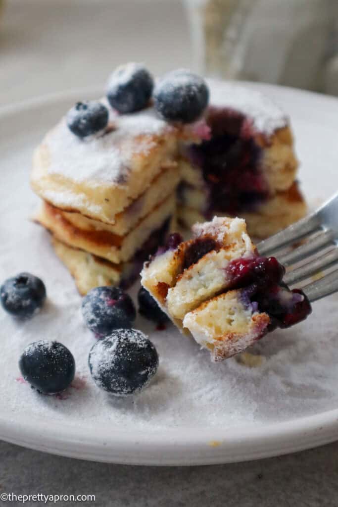 Bite of lemon ricotta blueberry pancakes on fork with fresh blueberries