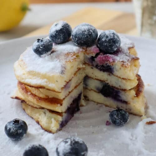 stack of four lemon ricotta blueberry pancakes with fresh blueberries and powdered sugar