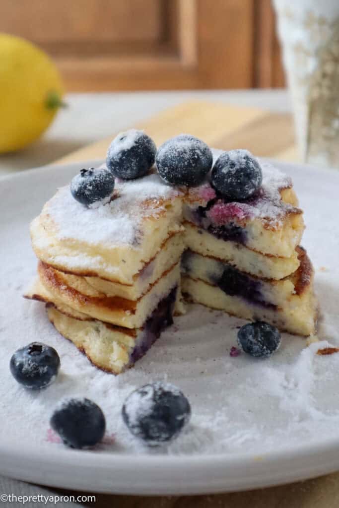 stack of four lemon ricotta blueberry pancakes with fresh blueberries and powdered sugar