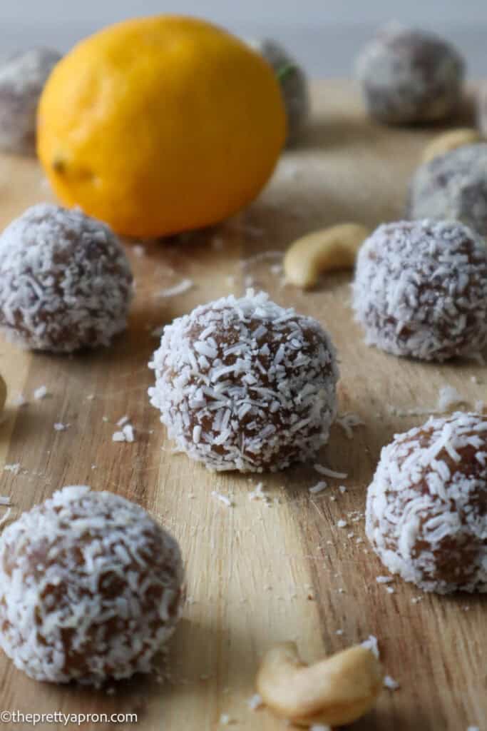 lemon bliss balls on wooden board with lemon and cashews