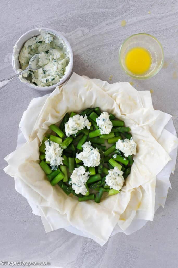 Small dollops of ricotta cheese on top of asparagus in quiche dish