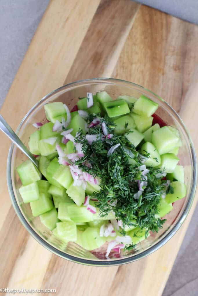 Diced cucumbers, chopped red onion and chopped dill in glass bowl