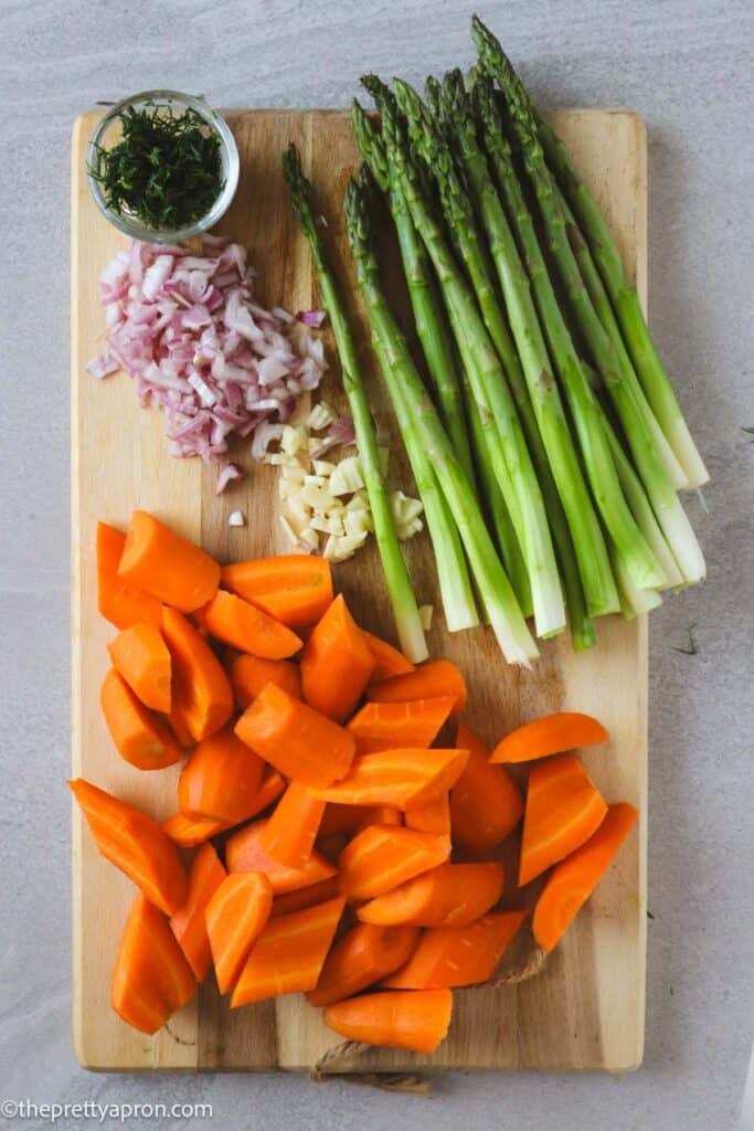 Chopped carrots, garlic, shallots, dill and asparagus on cutting board.