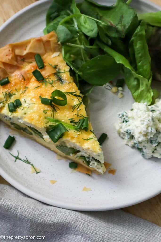 Slice of asparagus ricotta quiche with phyllo dough and dollop of lemon ricotta dip and green salad